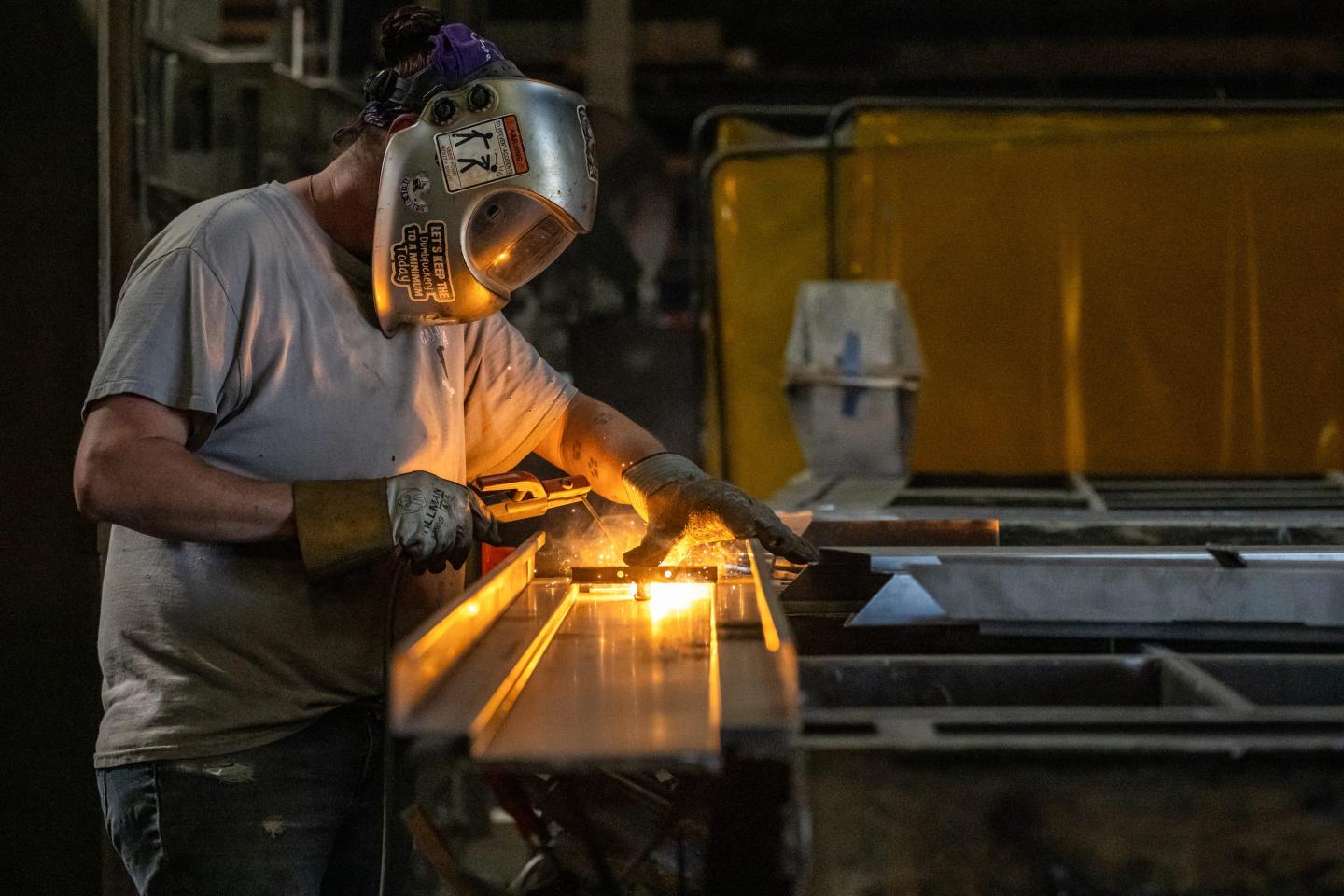 A person welds a piece of metal on a factory bench.