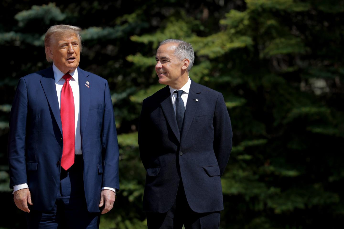Canadian Prime Minister Mark Carney smiles and looks to his right as he greets U.S. President Donald Trump, who stands straight and opens his mouth.