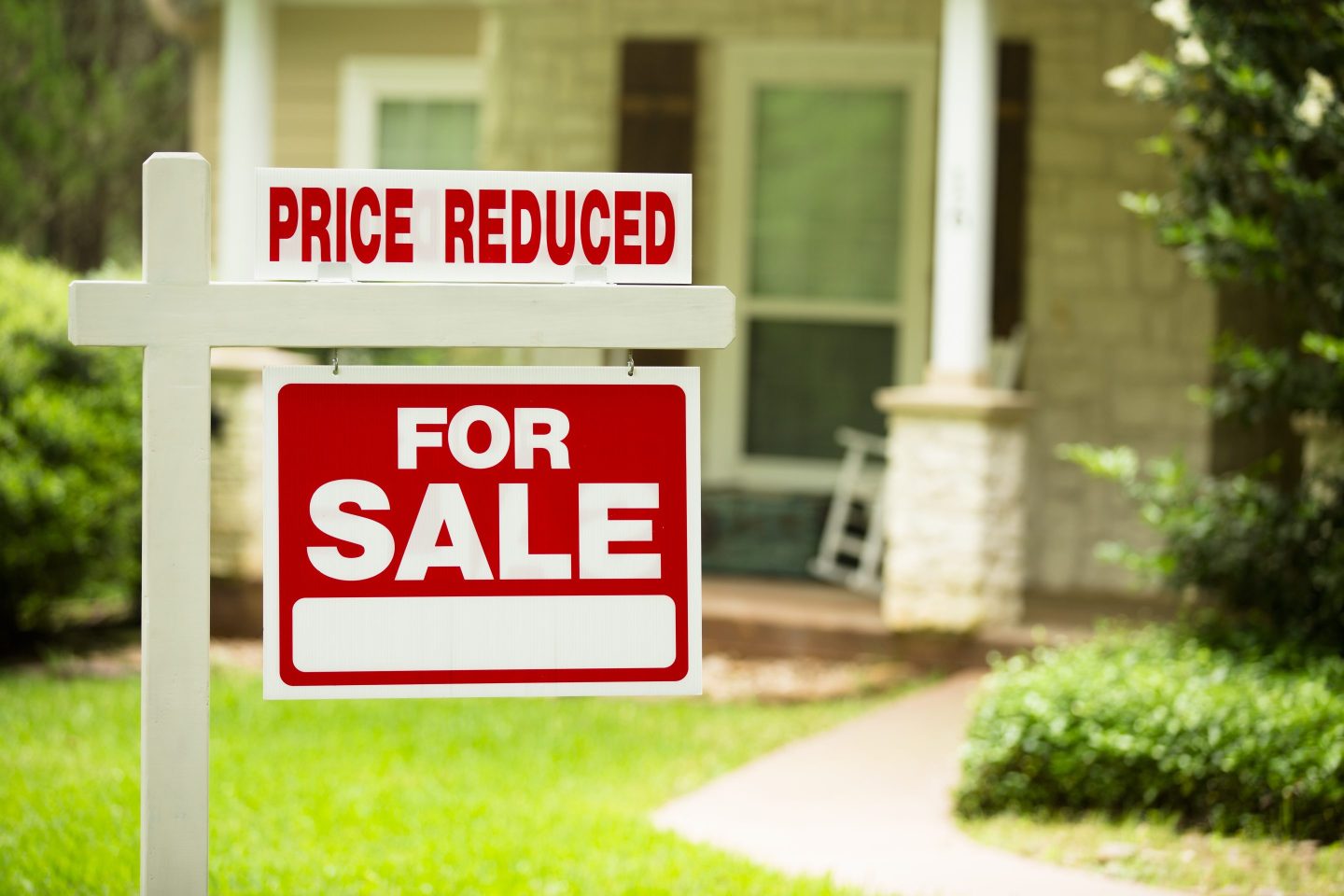 Photo of a for-sale sign in front of a home advertising "price reduced"