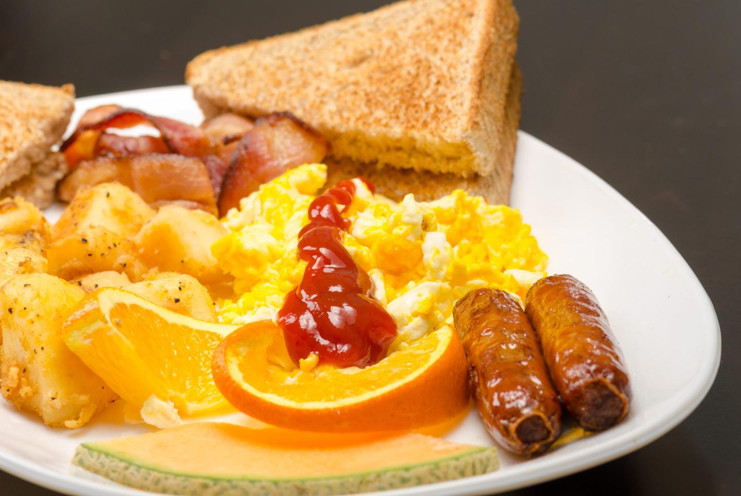 Ketchup adorns a plate of sausage, eggs, toast and a slice of orange