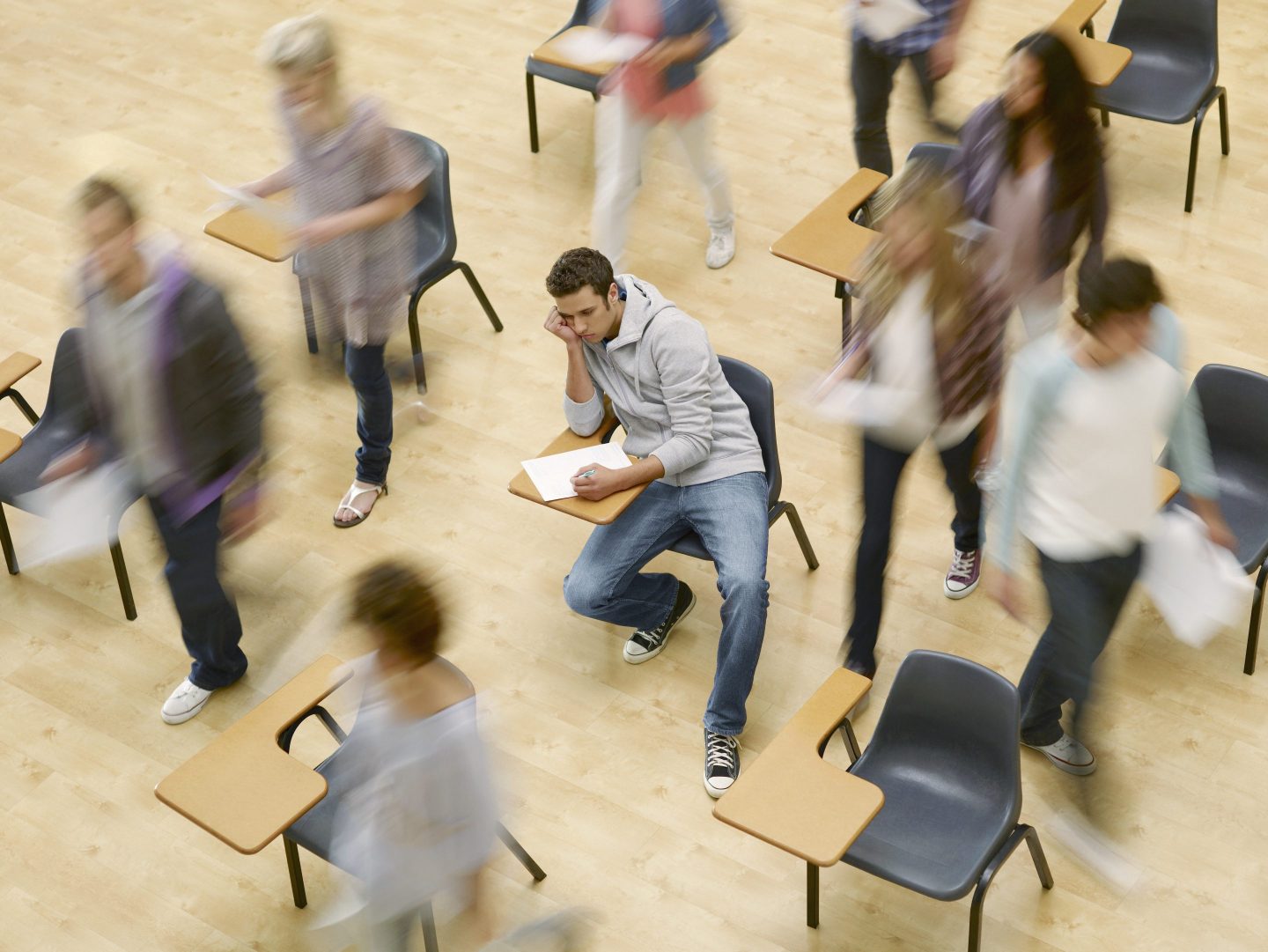College students moving around man at desk in classroom - stock photo
