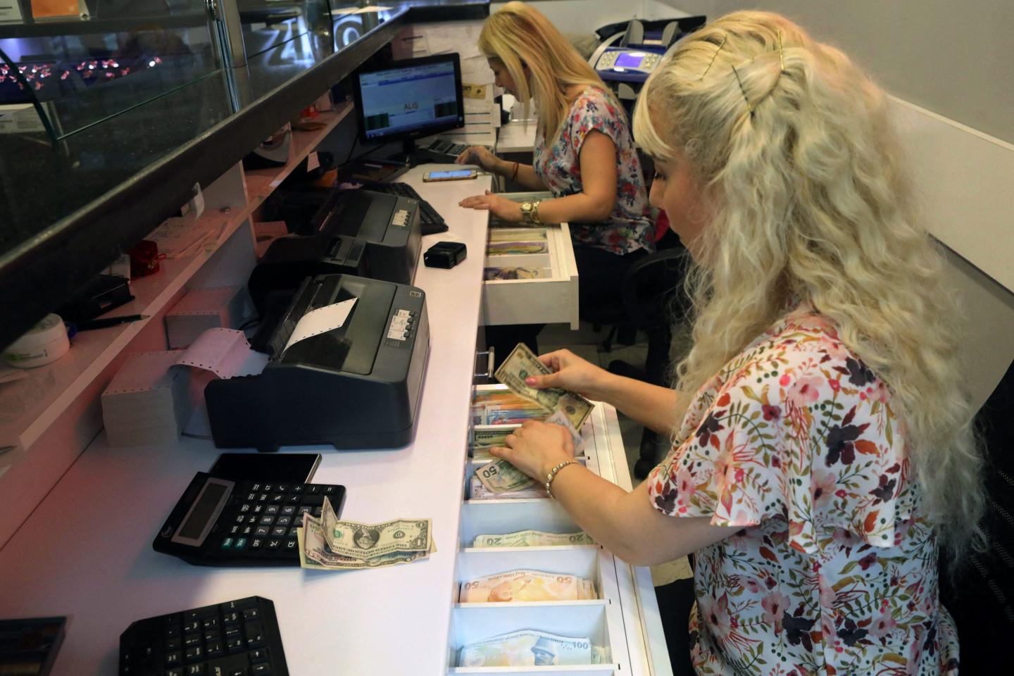 An employee in a foreign exchange office counts US dollars in front a teller's window.