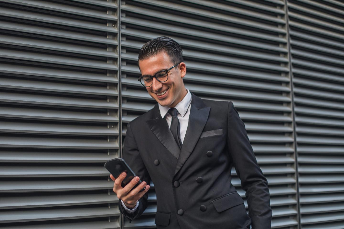 Business man stands outside looking down at this phone.