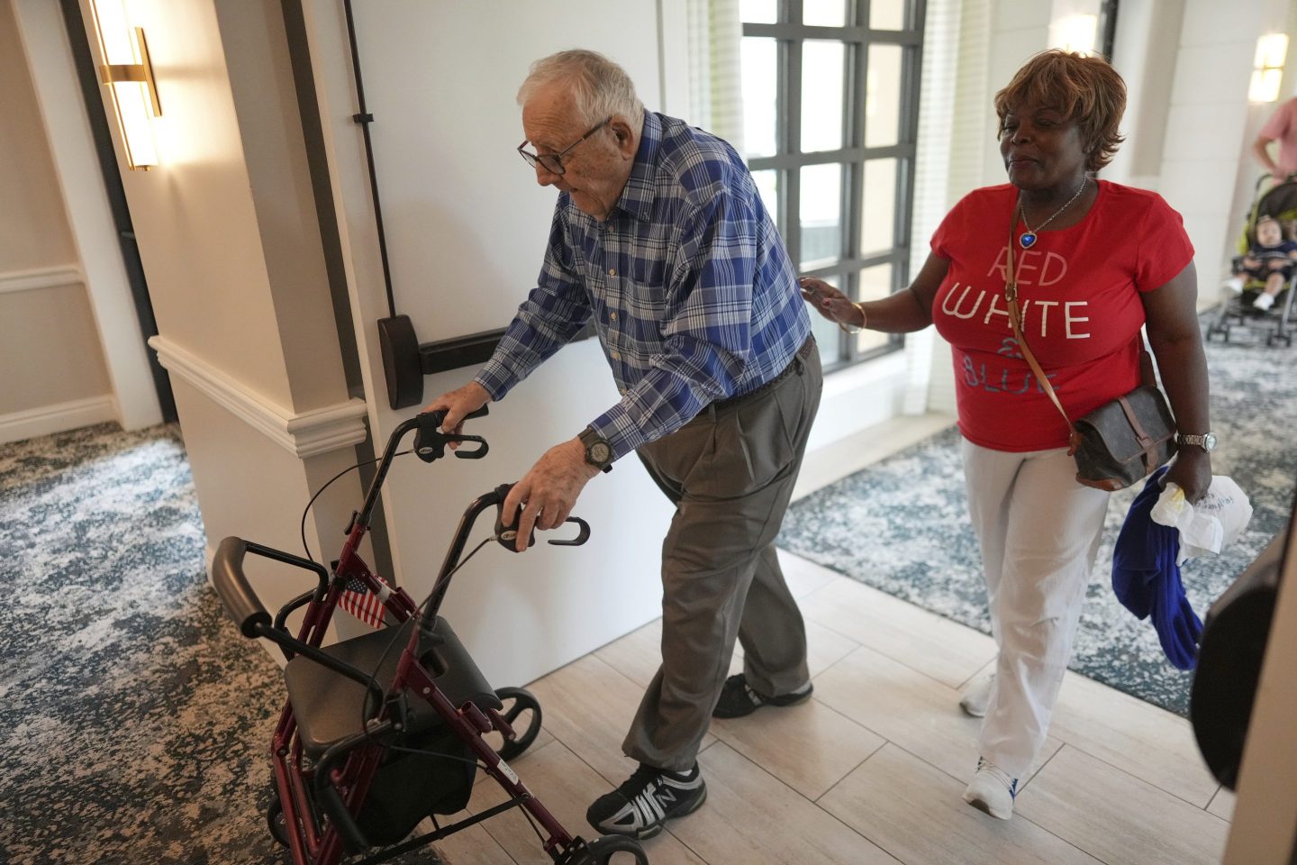 Resident Eugene Preslier, right, is accompanied by his private certified nursing aid Miriam Louis as he returns from a meal to his apartment in the independent living facility at the Toby and Leon Cooperman Sinai Residences, July 4, 2025, in Boca Raton, Fla.