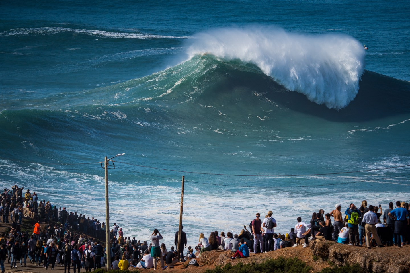 Photo: NAZARE, PORTUGAL - 2020/10/29: Despite the COVID-19 pandemic alert to social withdrawal, thousands of people attended the first big swell of the winter season in Praia do Norte. (Photo by Henrique Casinhas/SOPA Images/LightRocket via Getty Images)