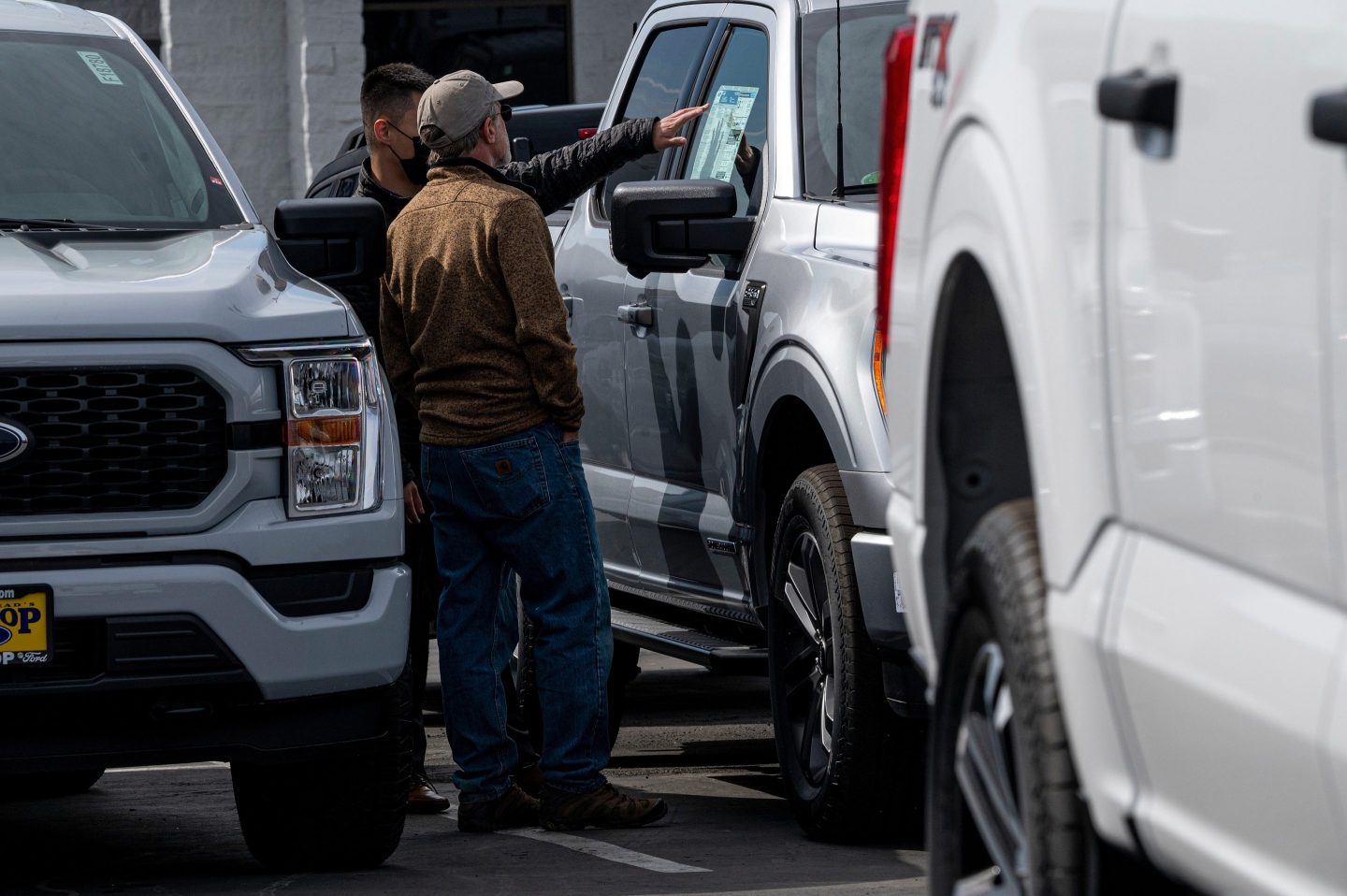 Two men look at a truck in a parking lot.