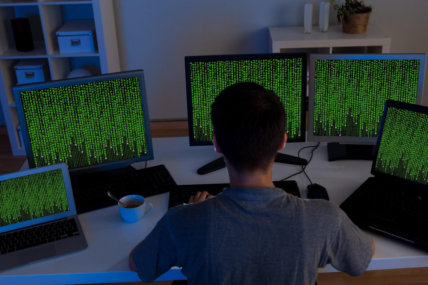 A man sitting at a desk with multiple screens showing green letters.