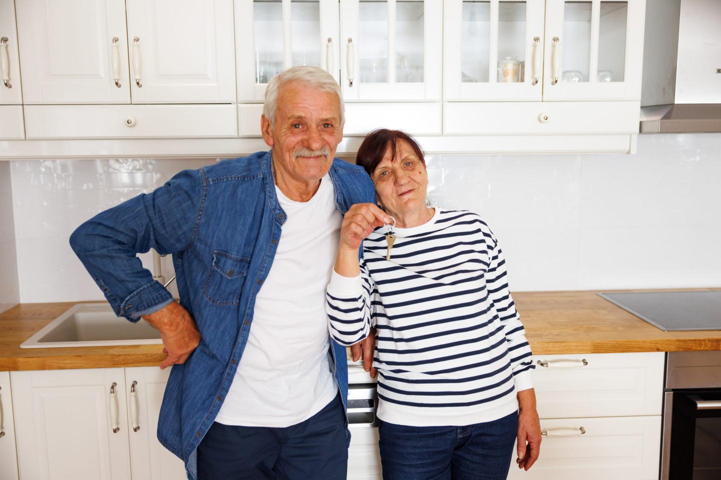 Old couple standing with keys to new home.