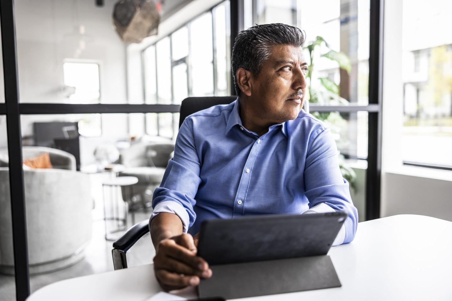 A man in front of a desk in an office looks out a window.