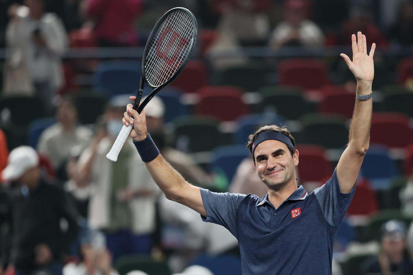 Roger Federer waves to fans, wearing a Uniqlo shirt and headband—and holding a tennis racket.