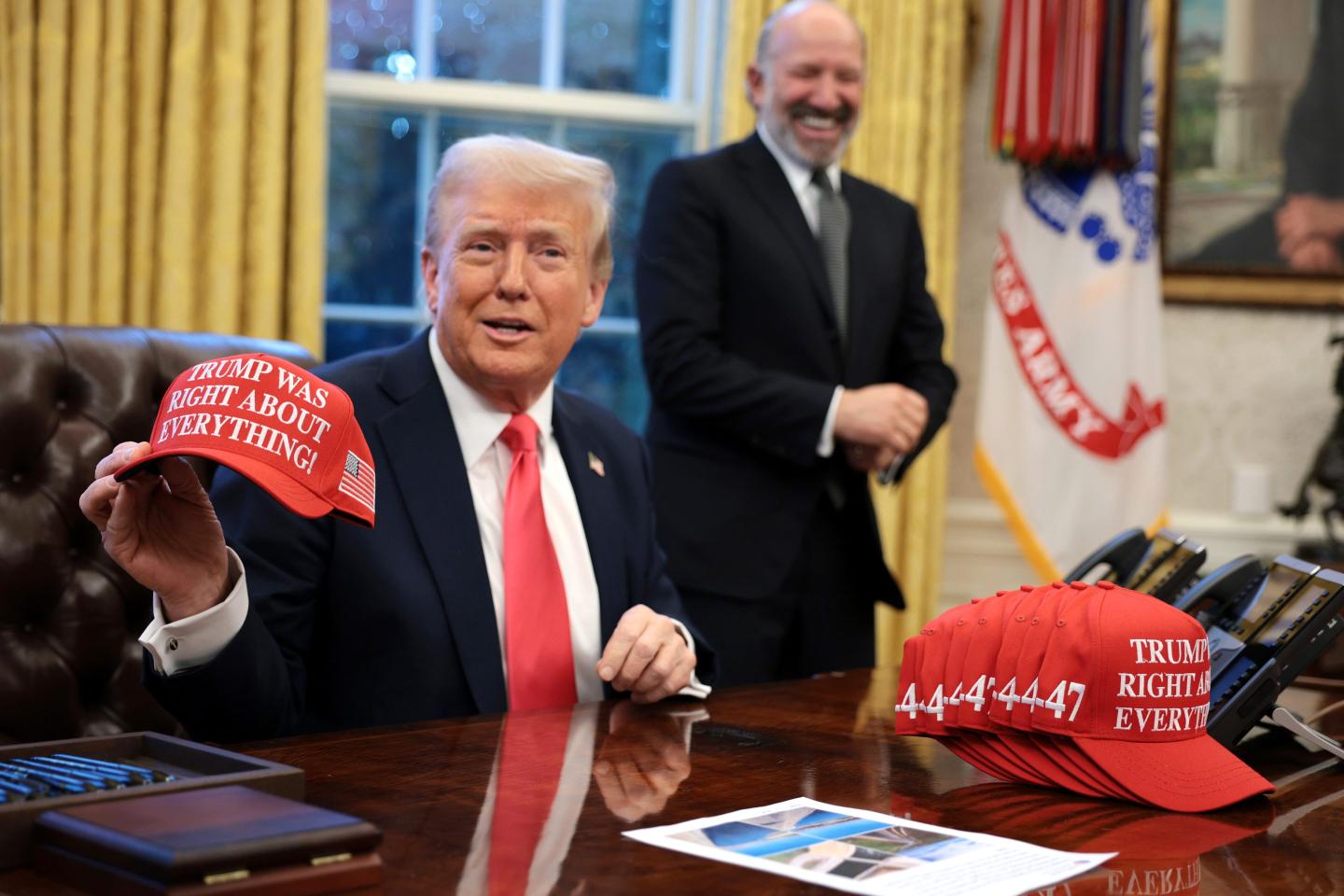Donald Trump, sitting in the Oval Office, holds up a red hat reading, "Trump was right about everything!"