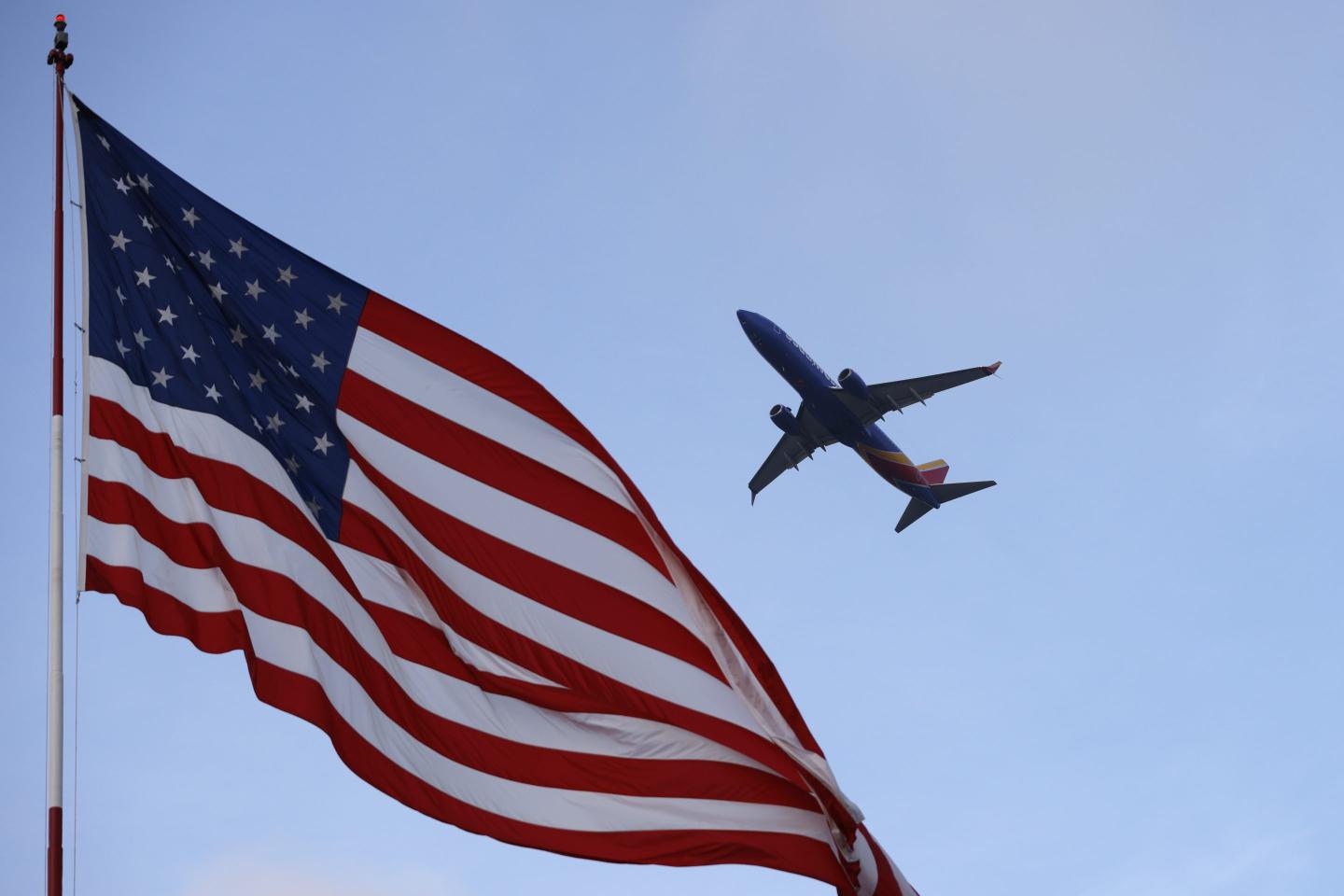 American flag blowing in the wind as an airplane flies in the sky above.