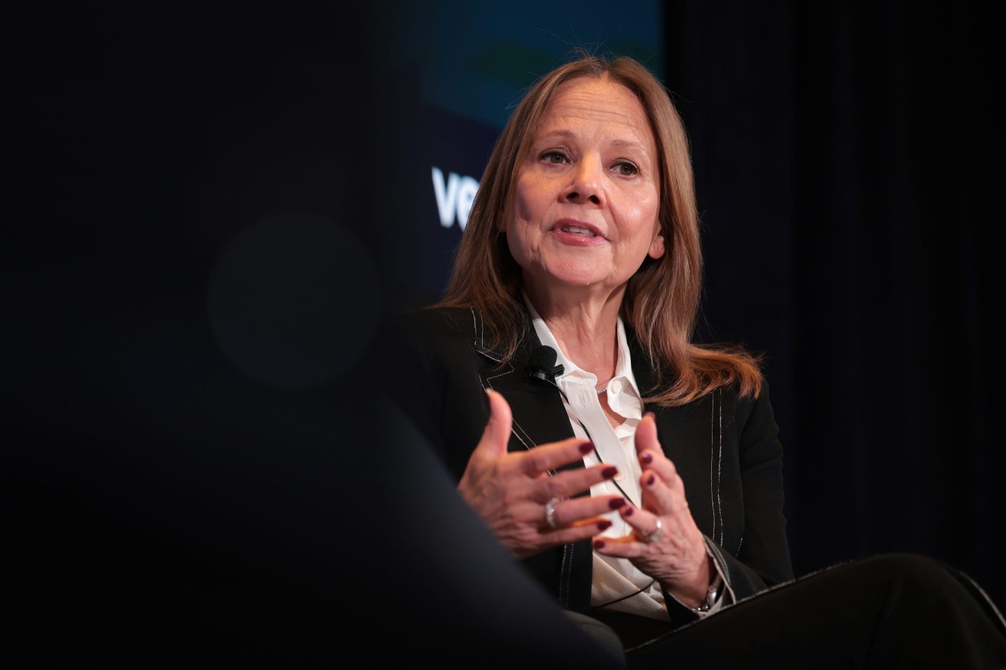 Mary Barra gestures and speaks in front of a black background.