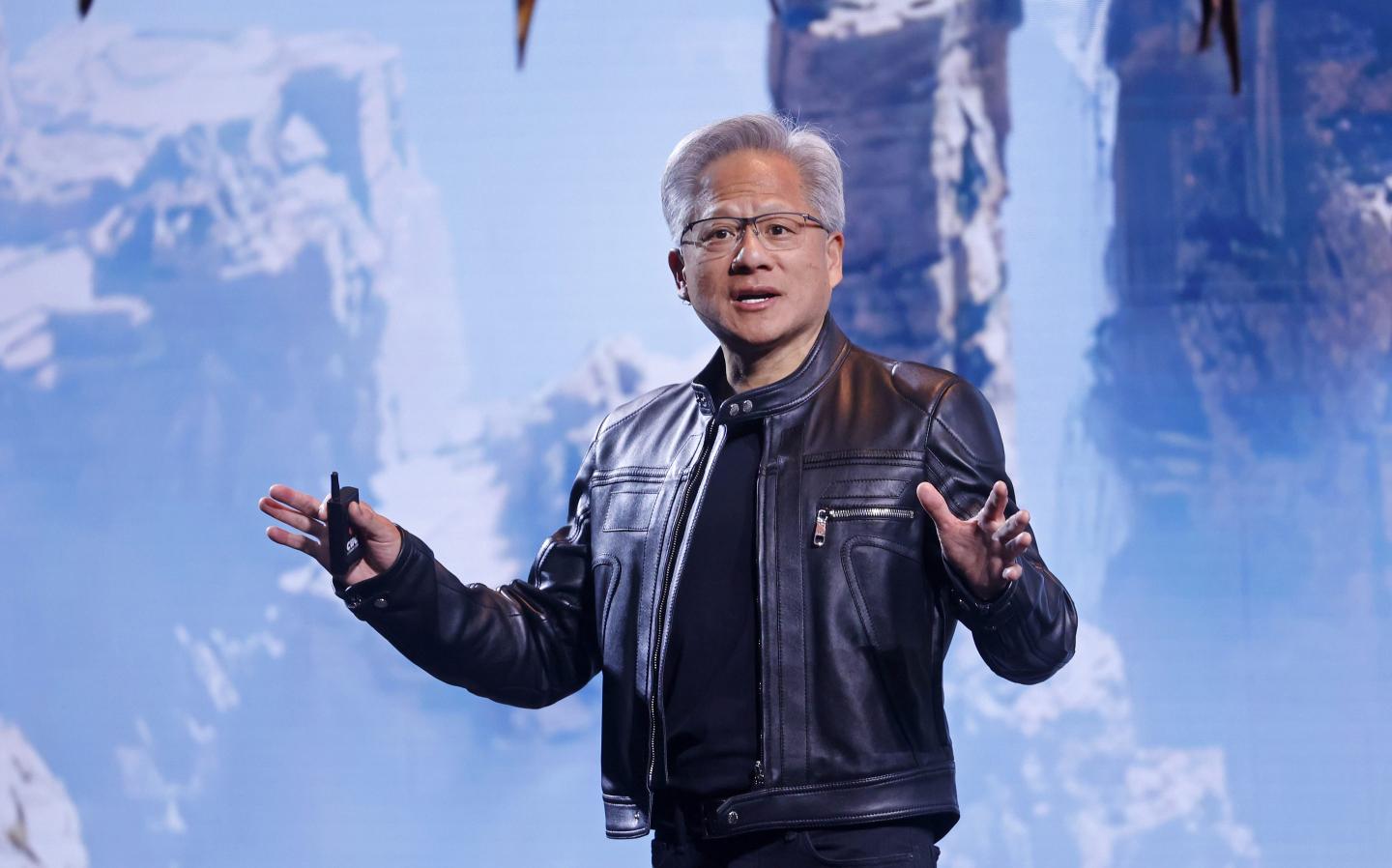 Jensen Huang, in a black leather jacket, stands on stage with a rocky mountain background projected behind him.