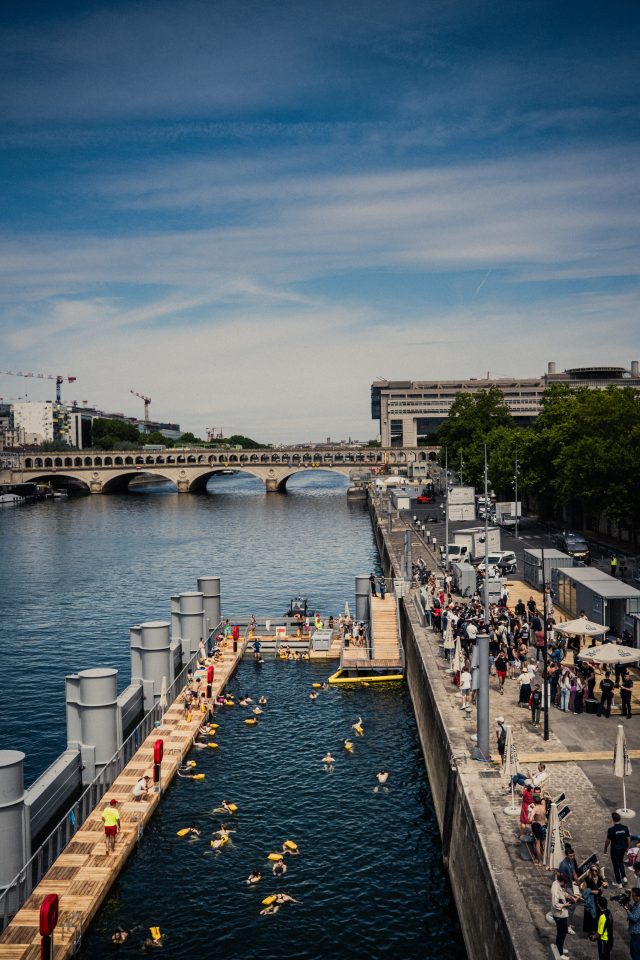 Far away, overhead view from the Passerelle Simone de Beauvoir of the first people swimming in the Seine at the safe bathing site at Bercy.