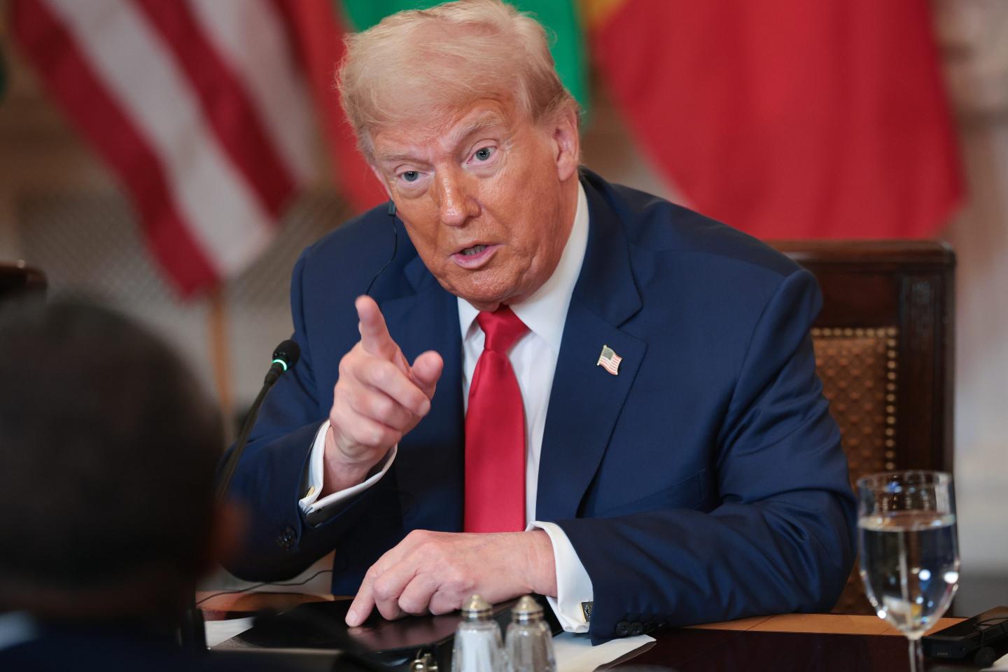 Donald Trump, sitting at his desk, point in front of him.