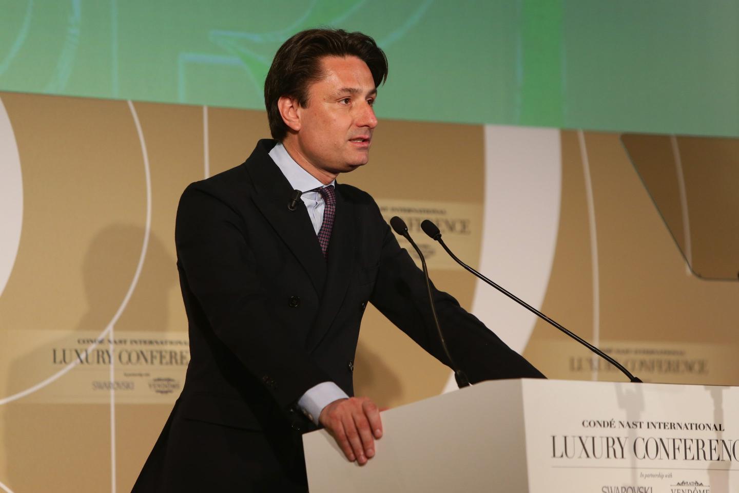 Axel Dumas, wearing a black suit, standing in front of a podium onstage