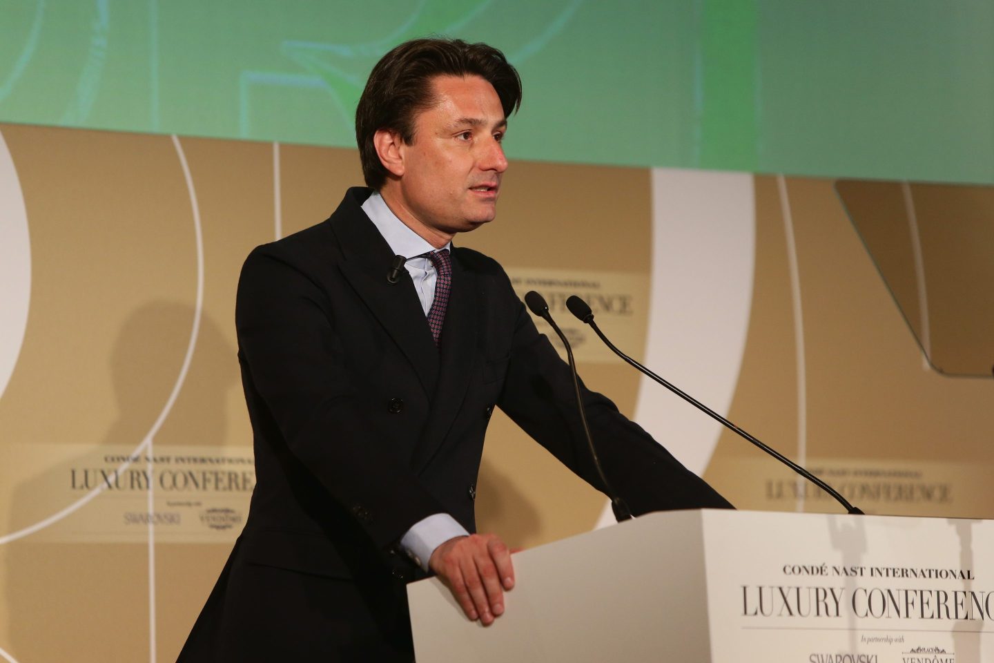 Axel Dumas, wearing a black suit, standing in front of a podium onstage