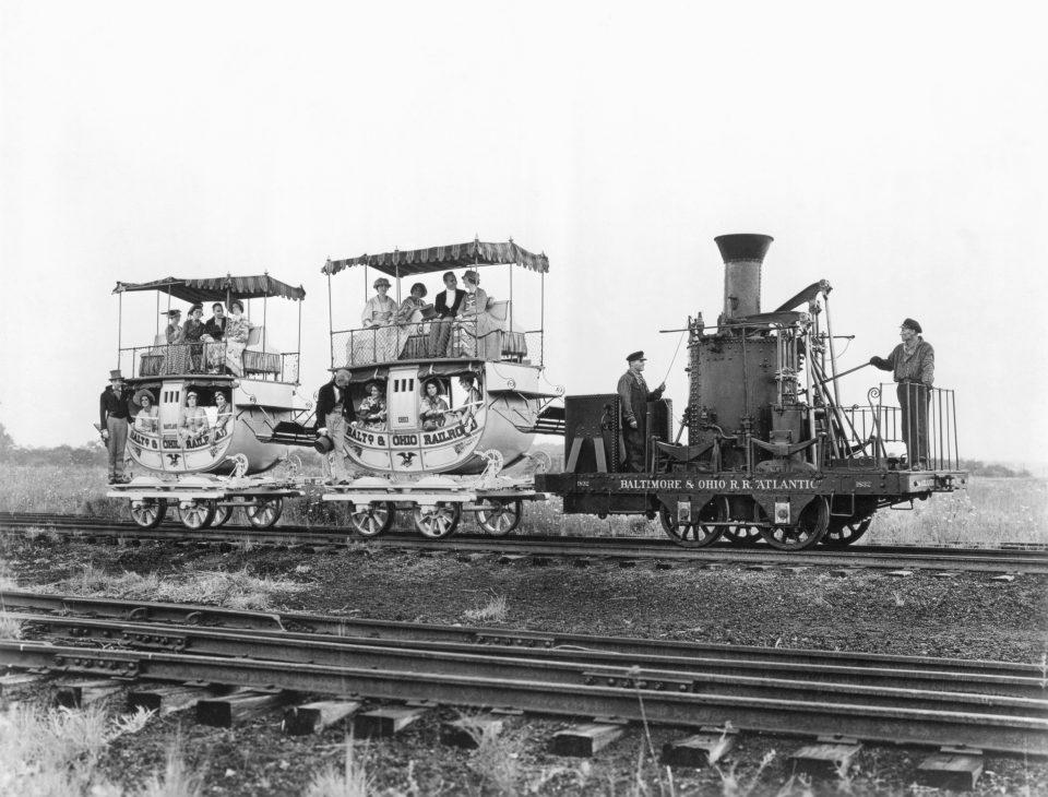 The "Atlantic" locomotive pulling two double-decked Imlay coaches full of people.