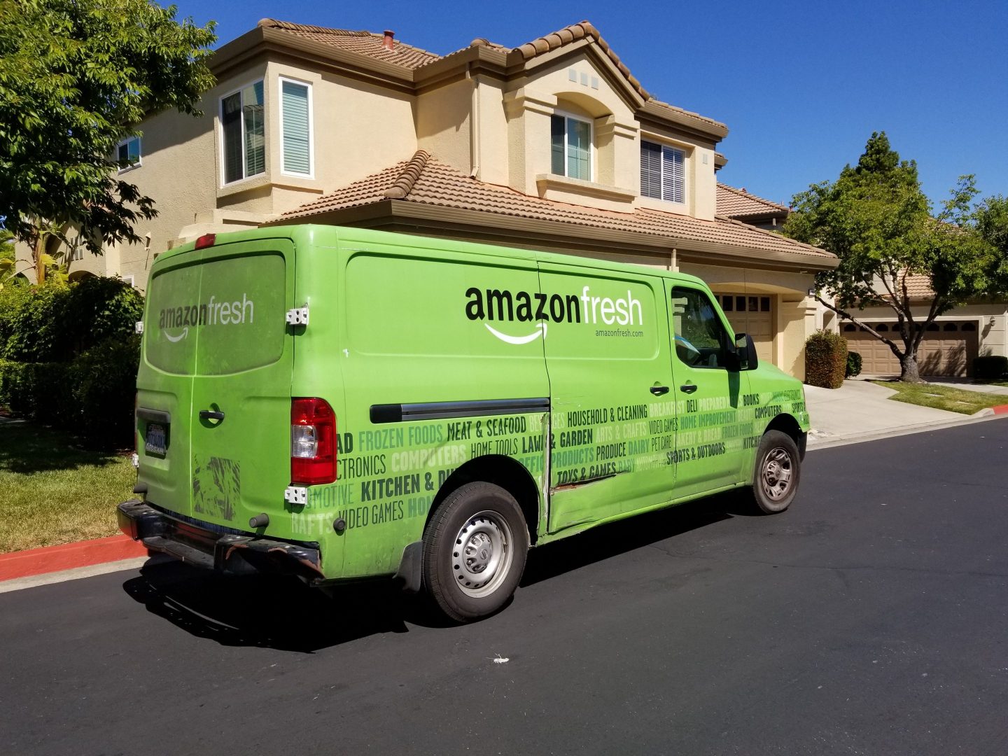 A green Amazon Fresh truck parked in front of a house