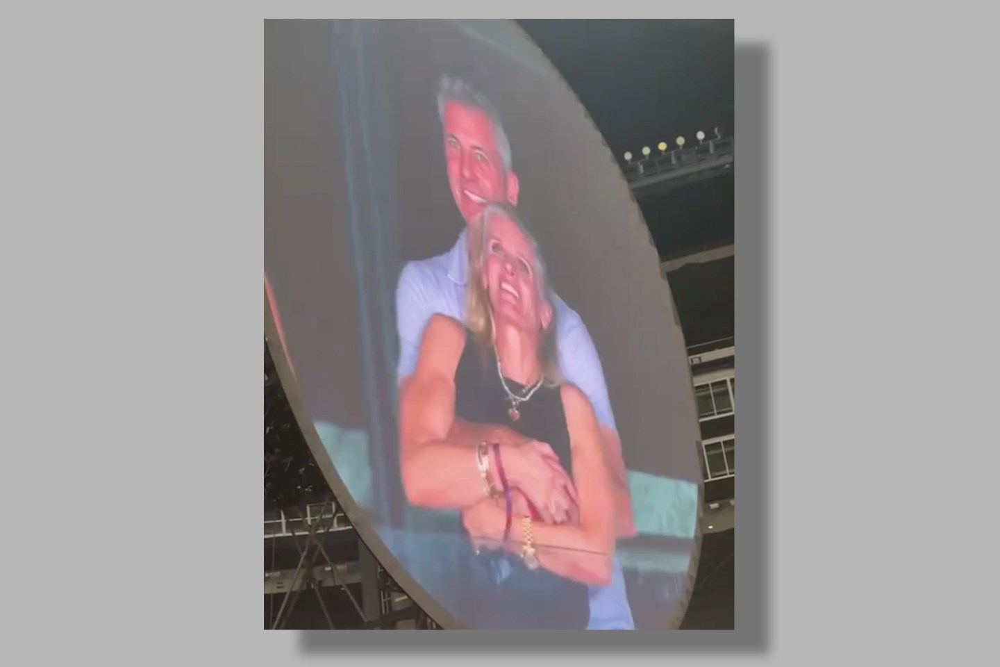 A man on a jumbotron hugging a woman from behind.