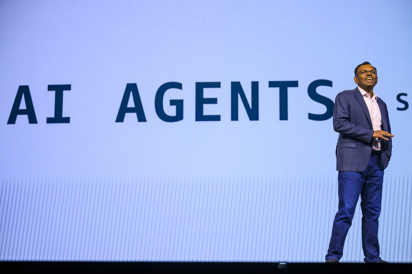 An Amazon executive appears onstage at an event with the words AI AGENTS on a screen behind him
