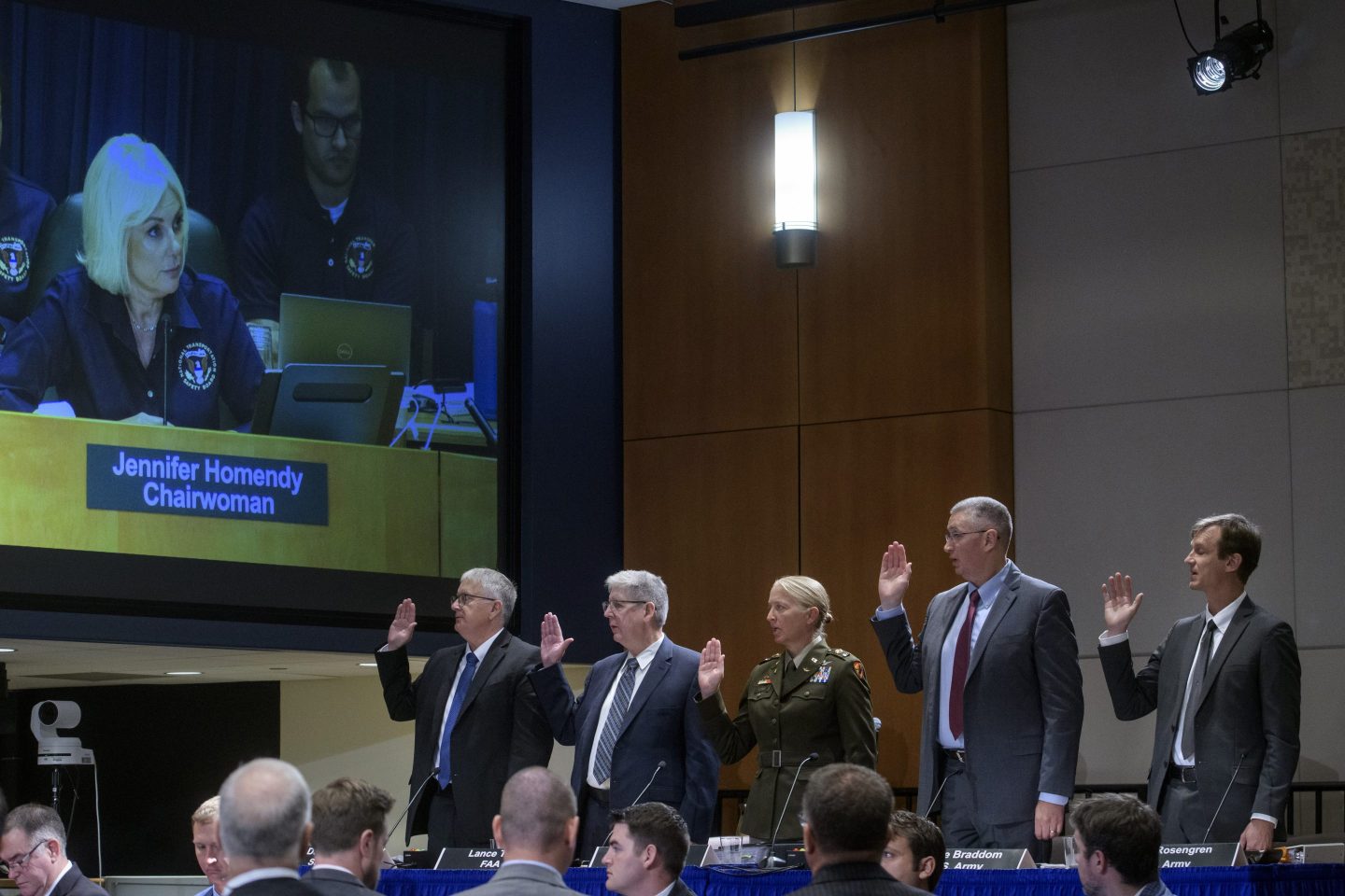 National Transportation Safety Board Chairwoman Jennifer Homendy, on monitor left, swears-in the witnesses from left: Dan Cooper, Sikorsky Aircraft, Lance Gant, Federal Aviation Administration, U.S. Army CW4 Kylene Lewis, Steve Braddom, U.S. Army, and Scott Rosengren, U.S. Army, during the NTSB fact-finding hearing on Wednesday.