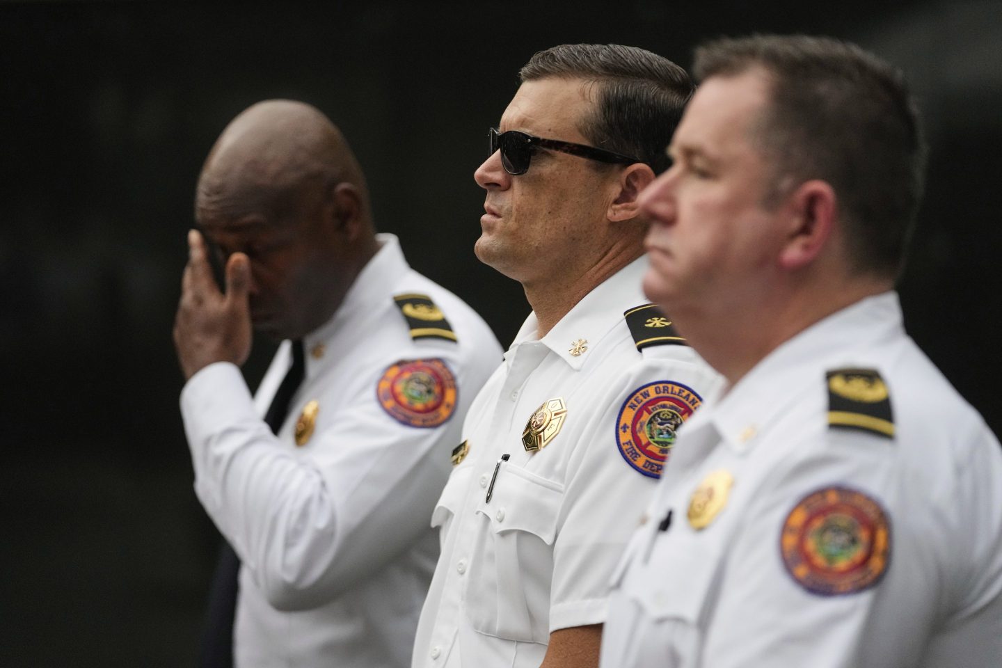 New Orleans fire chiefs Zachary Gremillion, left, Ray Casey, and Byron Casey, right, stand at attention in an emotional moment.