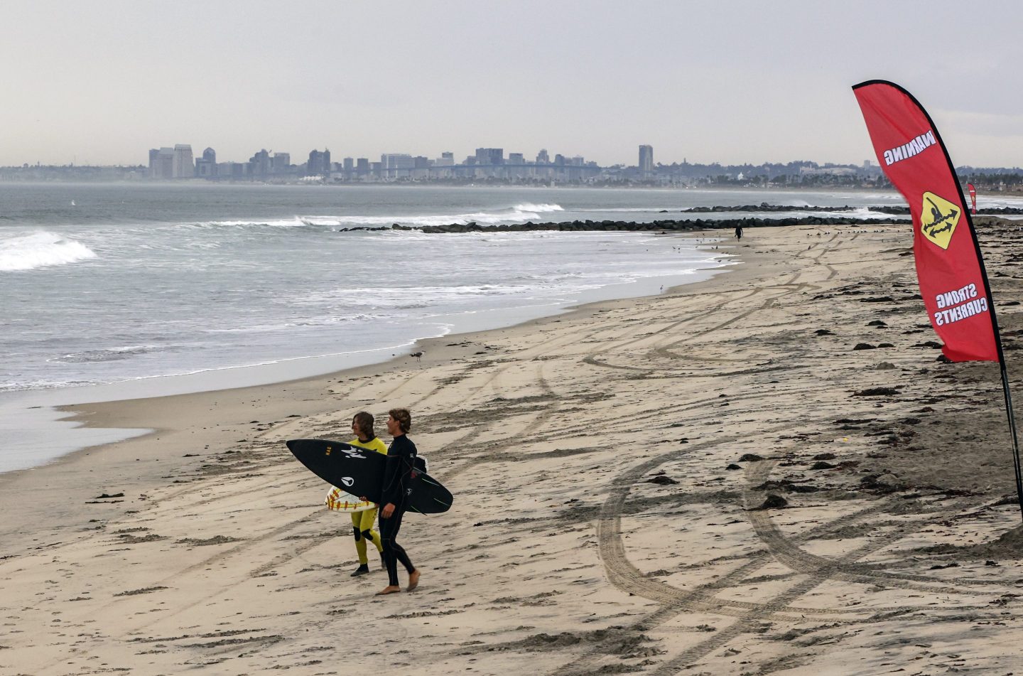 Surfers walk past a flag warning of strong currents just north of the Imperial Beach Pier on Sept. 9, 2022, in Imperial Beach, Calif.