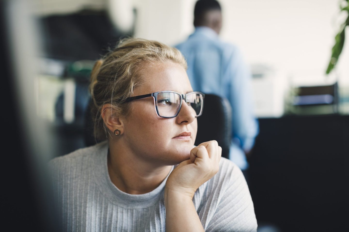 A woman sitting in an office looks to the side, disappointed.