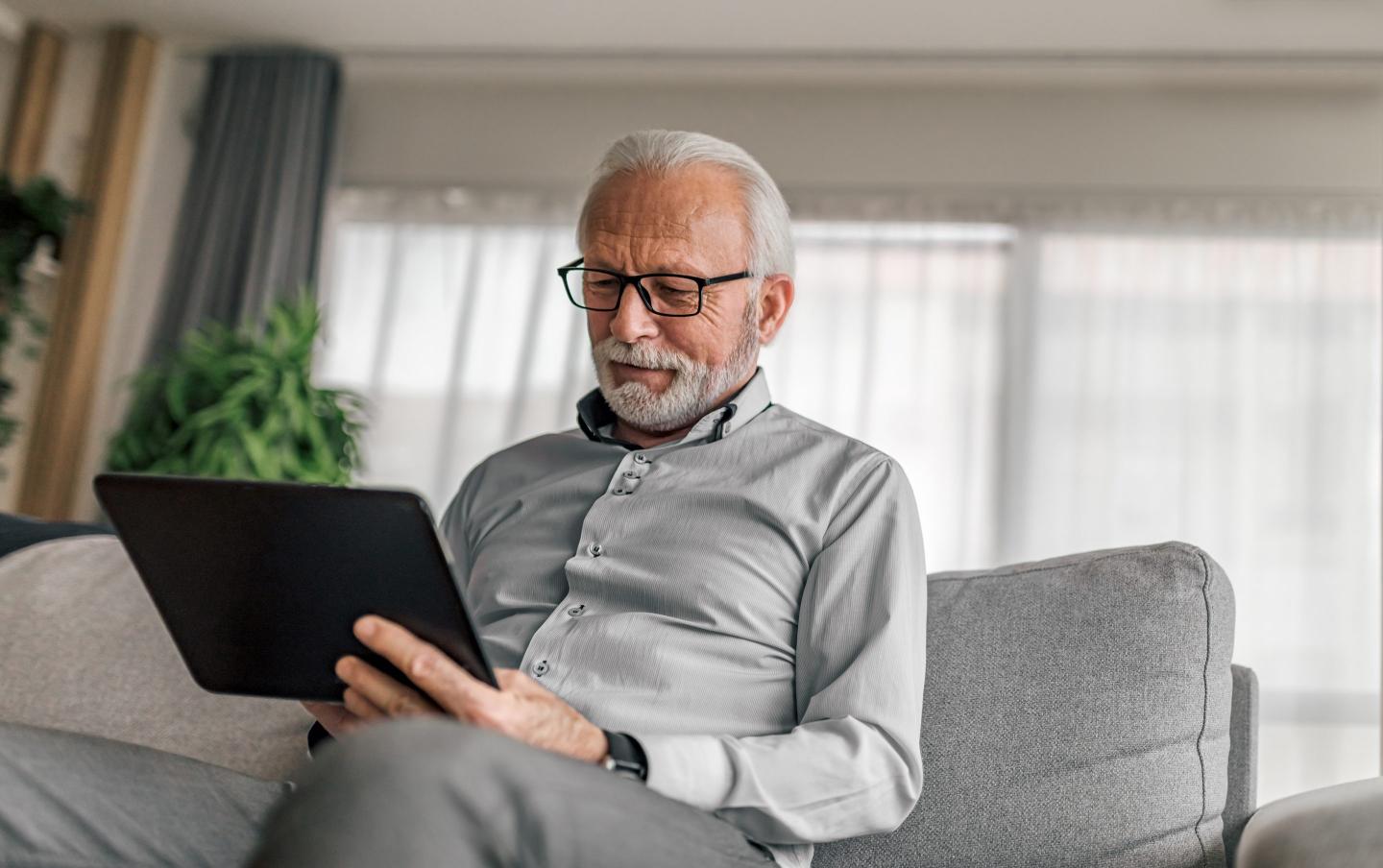 An old man holding a tablet sitting on a couch