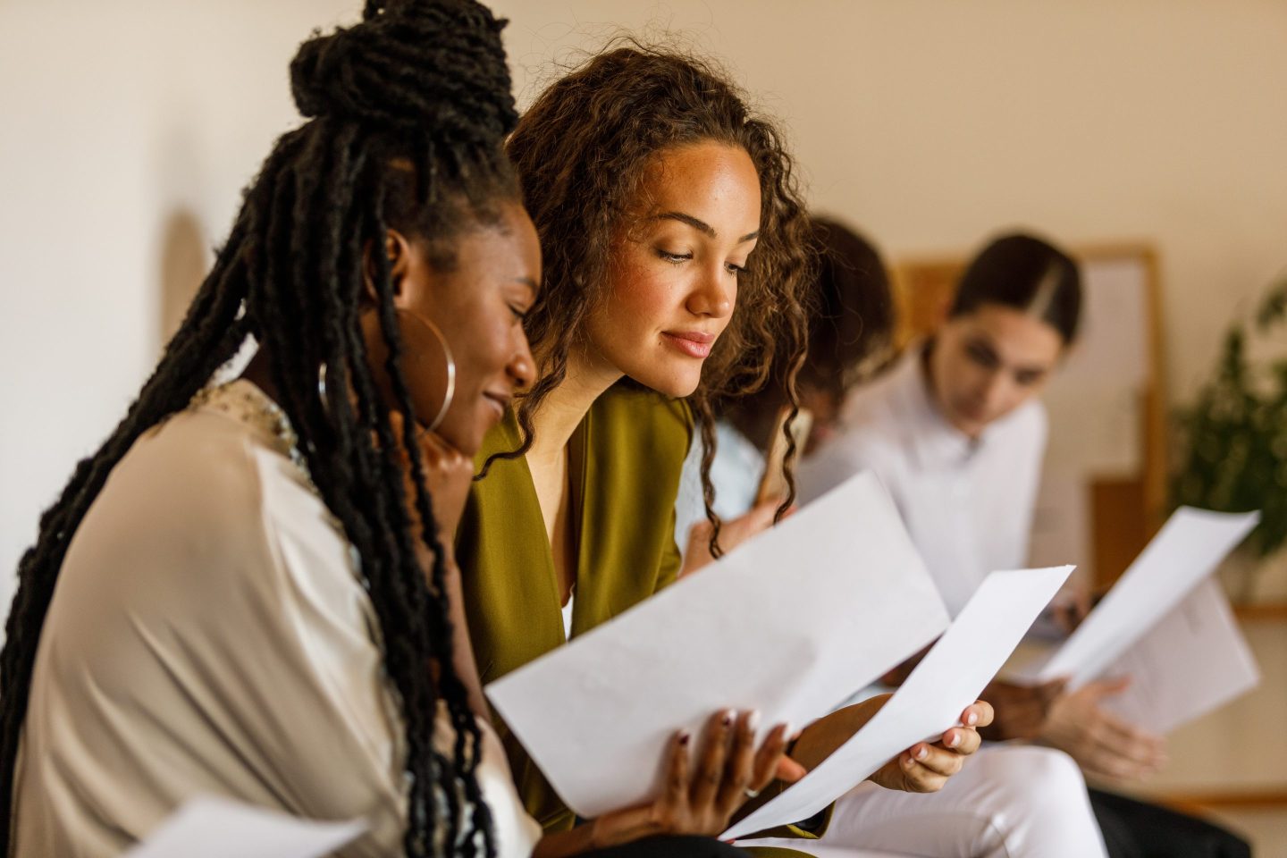 Young professionals sit in line against the wall, chatting, preparing and reading their resumes and cover letters when waiting for a job interview.