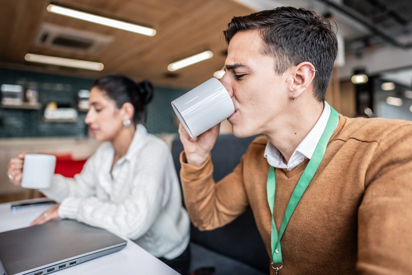 A millennial drinks a coffee at his desk