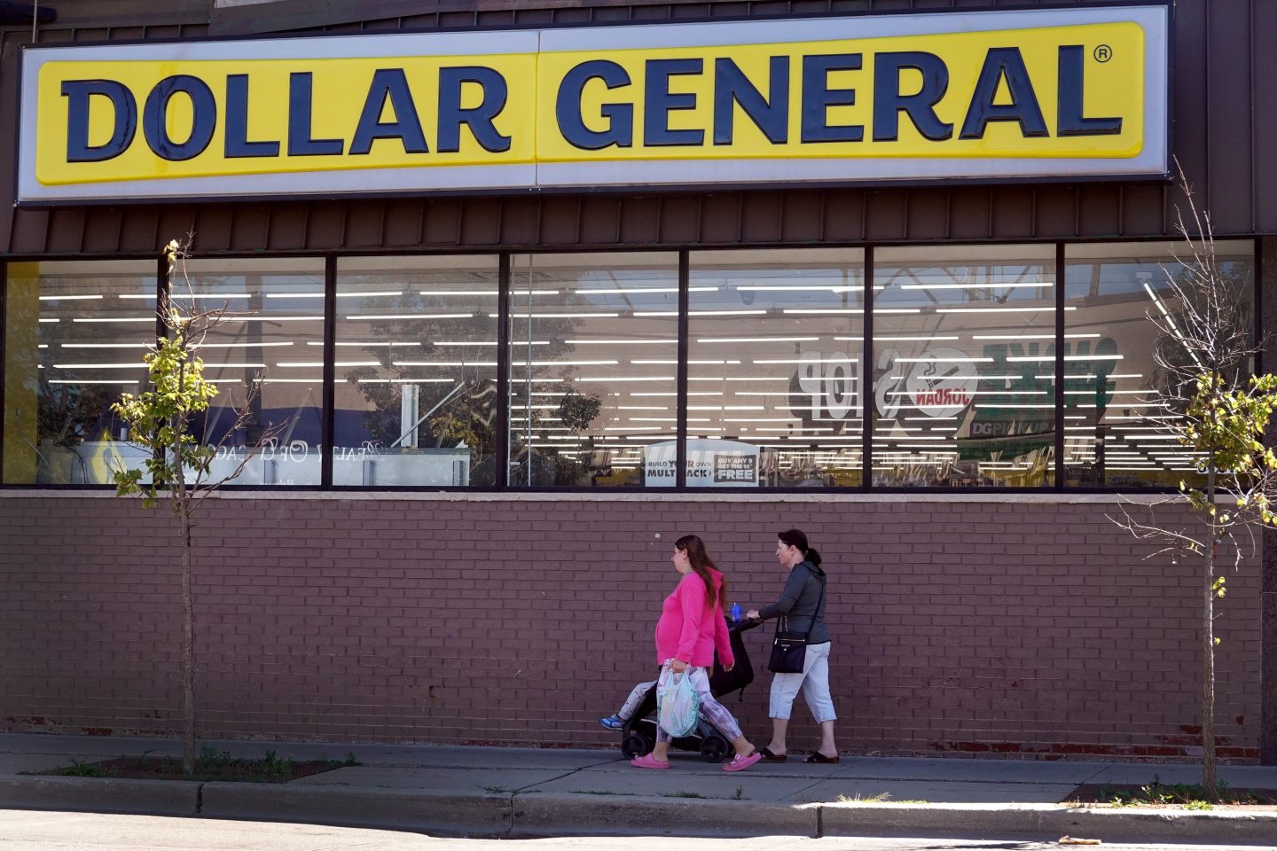 Two women walk under a Dollar General sign.