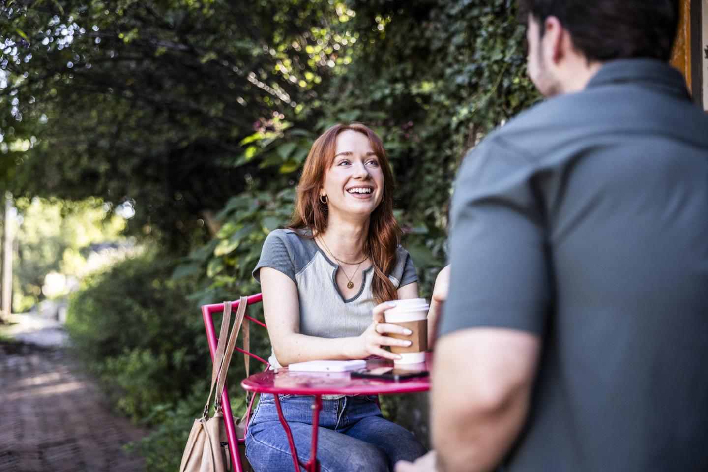 A woman sits at a red table outside and looks at a man sitting across from her.