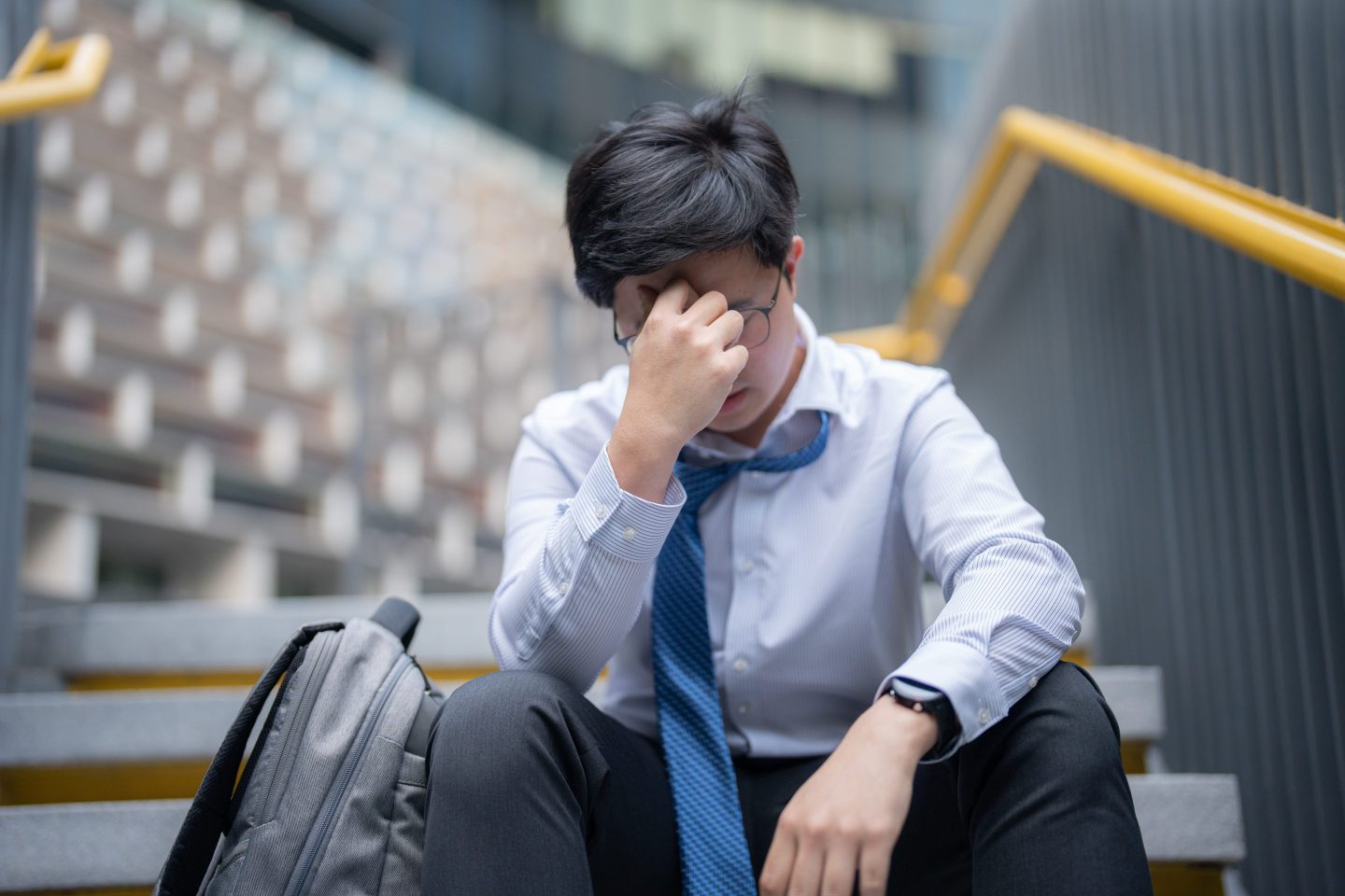 A young, anxious businessman with his head in his hands, sitting outside his building