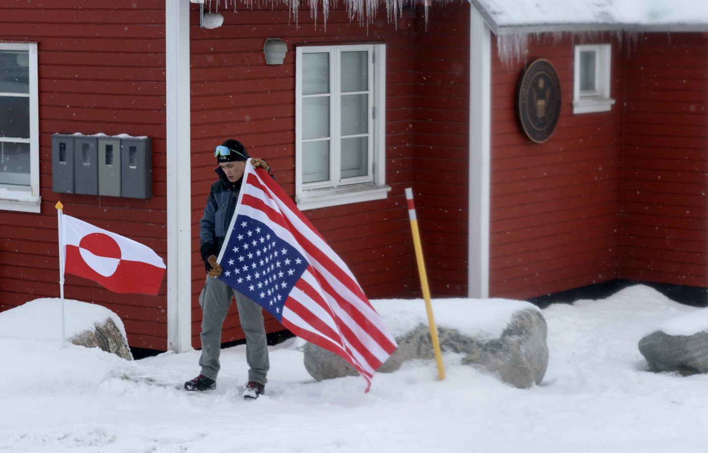 A greenlander on a snowy day hoists the American flag upside down next to the Greenland flag.