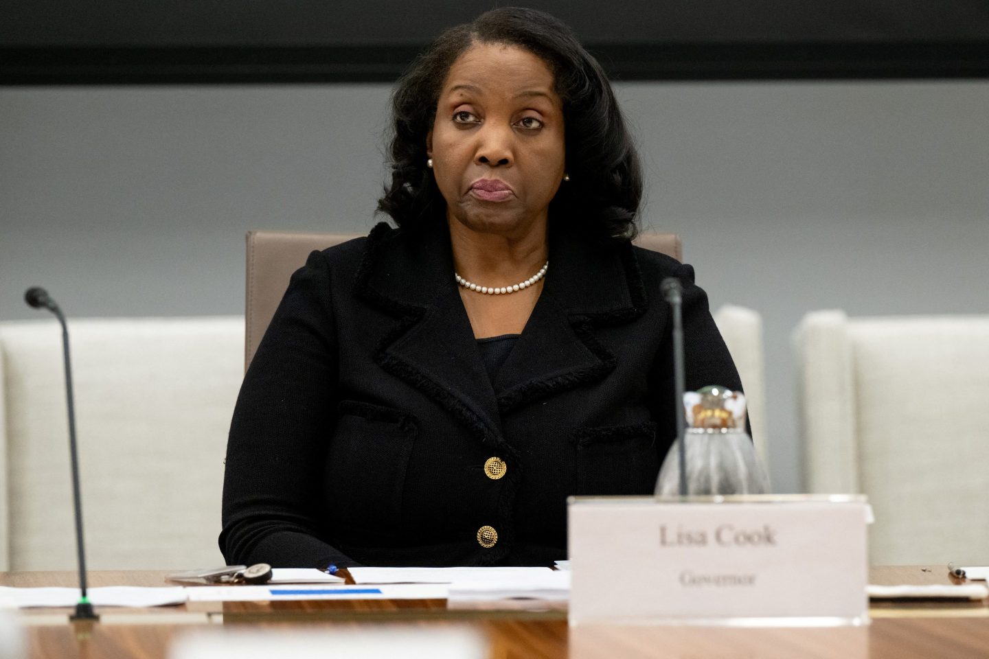 Lisa Cook, member of the Board of Governors of the US Federal Reserve, attends a Federal Reserve Board meeting and sits with pursed lips in a black suit.