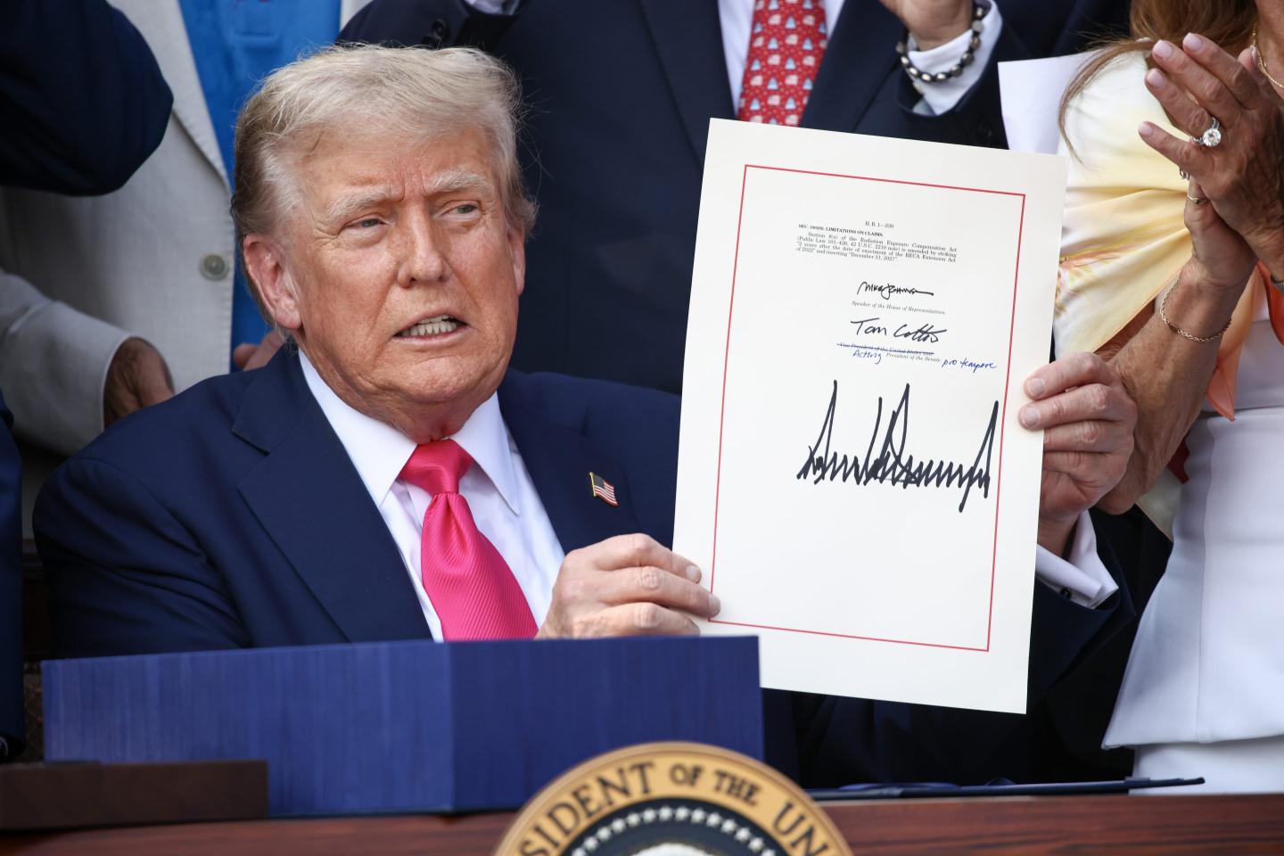 President Donald Trump holds up a sheet of paper with his signature on it.