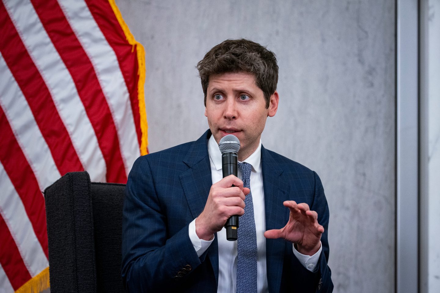 Sam Altman speaking into a mic in front of the US flag.