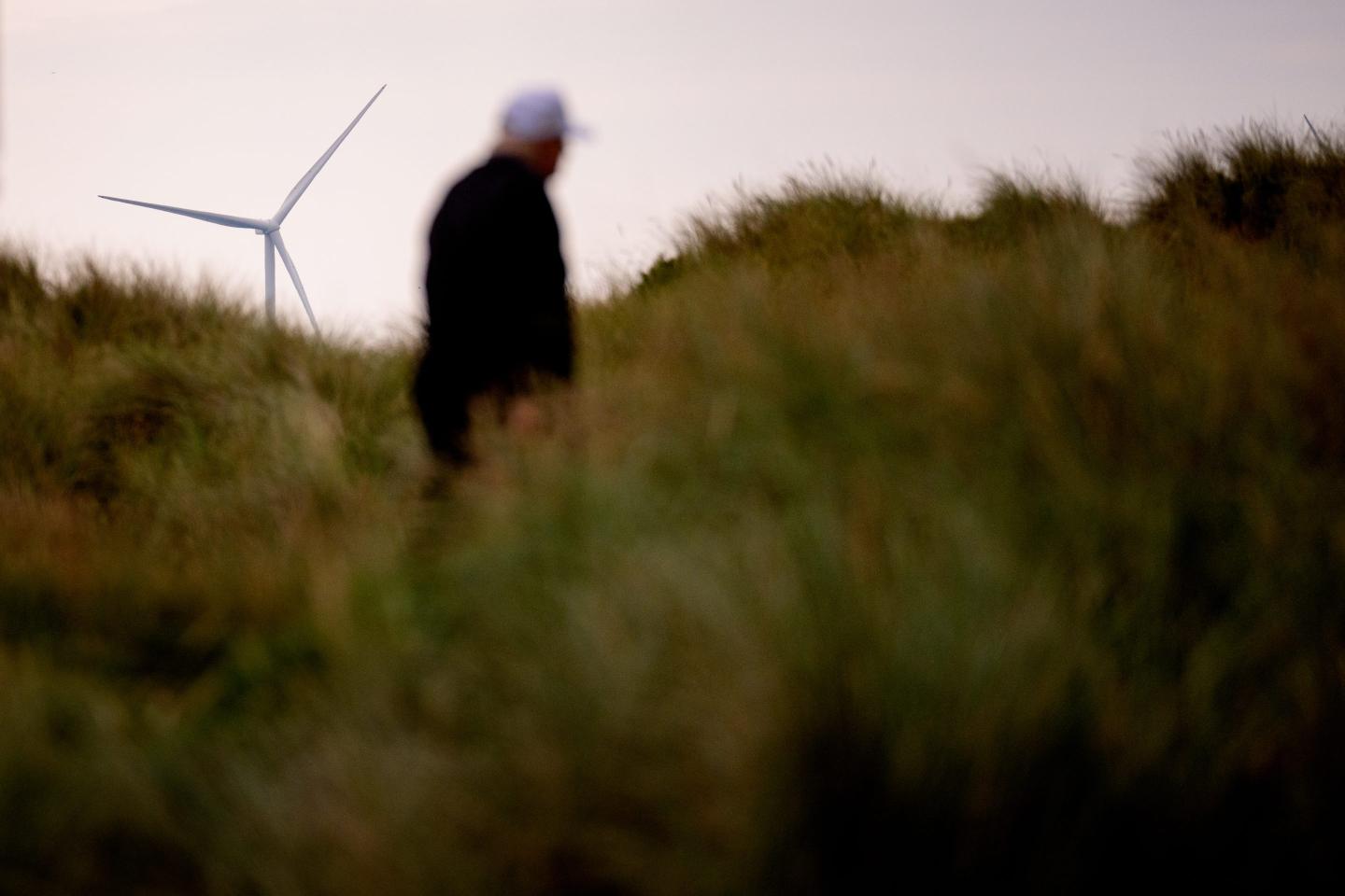 A blurred trump walks in front of a wind turbine.