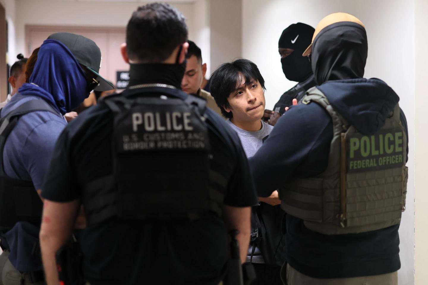 A man is surrounded by ICE agents who appear to be detaining him.