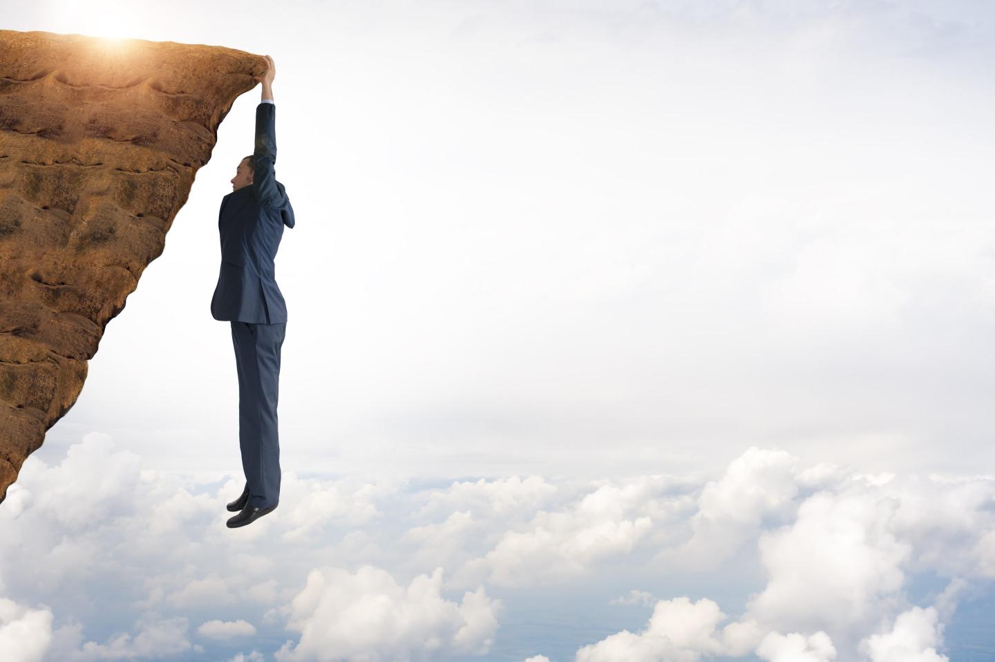 Photo of a businessman clinging to the edge of a cliff