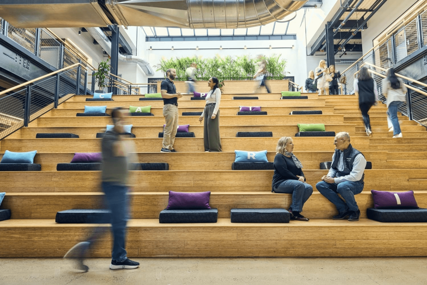 Employees walk and talk on benches in an office space.
