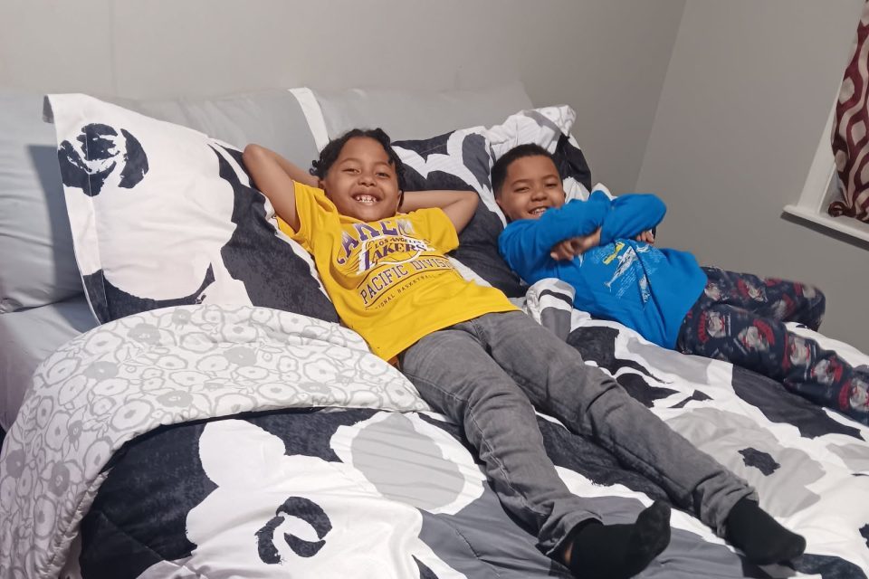 Two brothers lay on top of a freshly made bed smiling