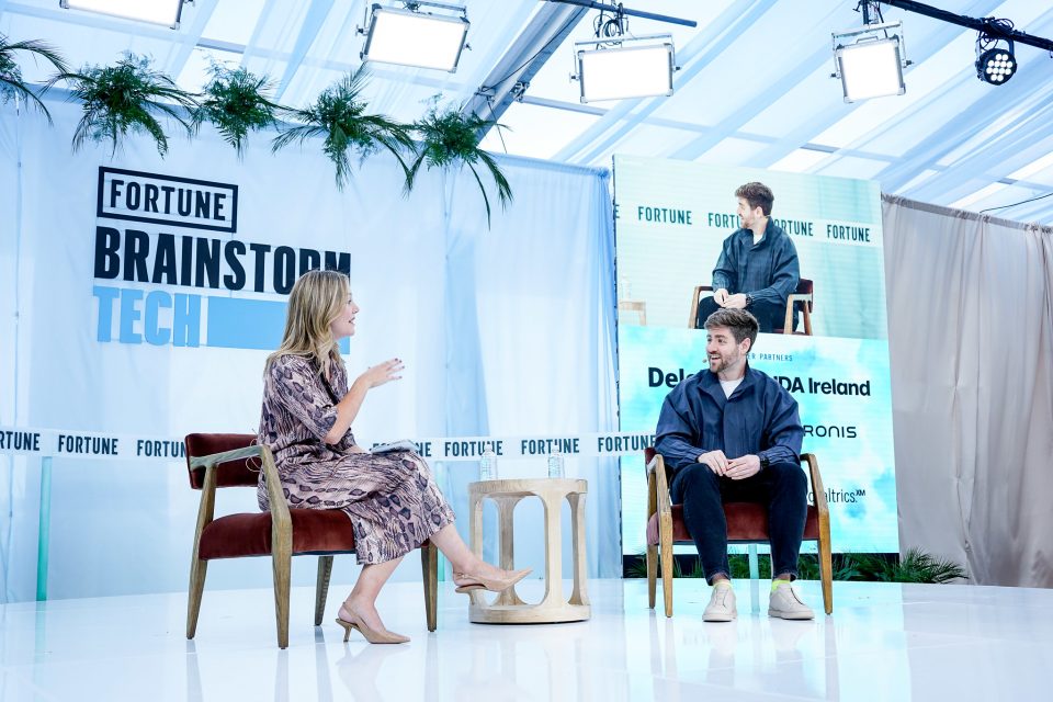 Two people sit facing each other on a stage with a banner reading "Fortune Brainstorm Tech" in the background.