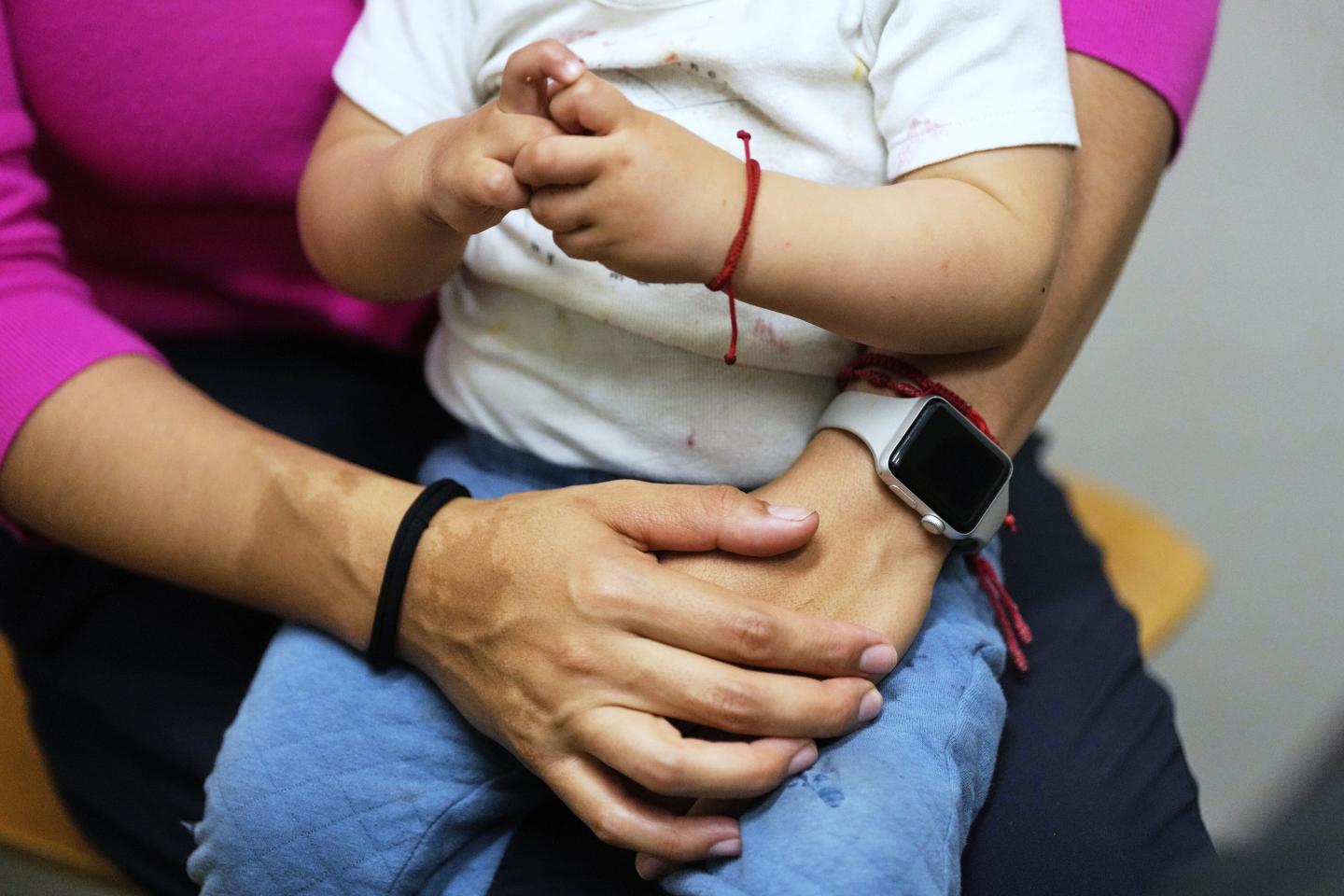 A small child is shown on his mother's lap, with her arms around him, as they wait at a clinic.