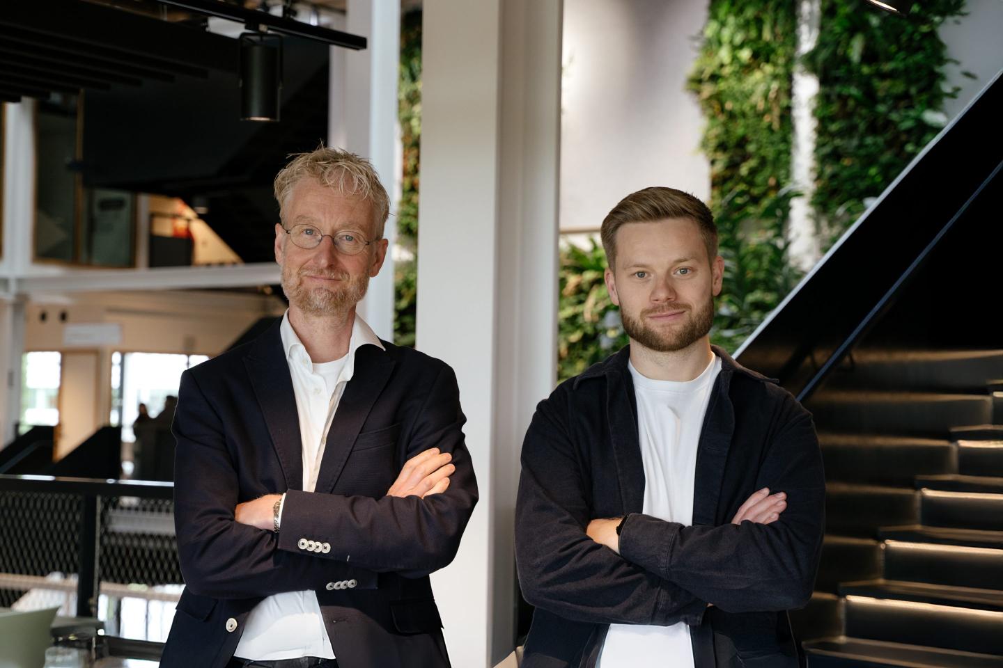 CuspAI cofounders Max Welling (left) and Chad Edwards, standing with their arms crossed in matching white T-shits and black jackets.