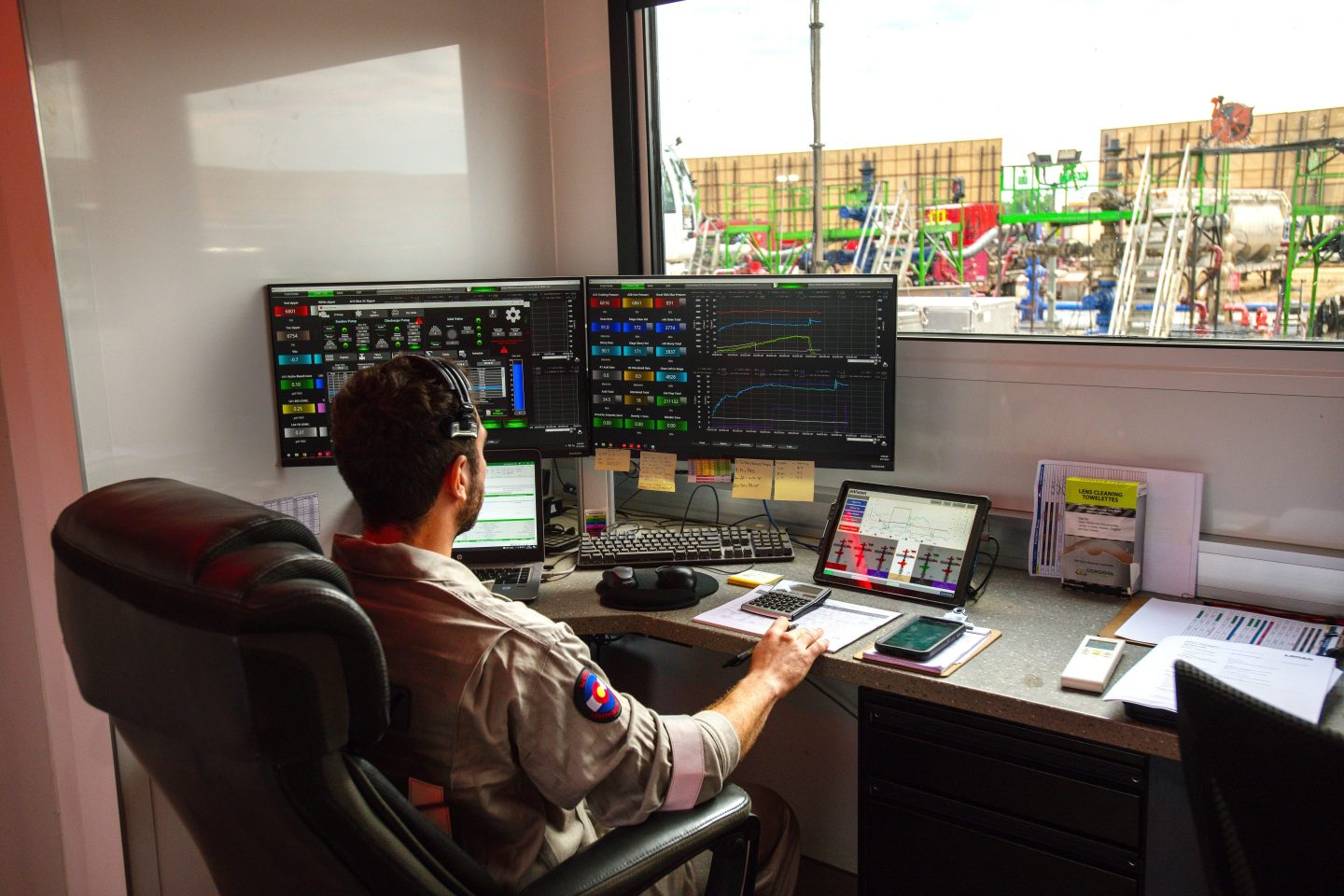 A Liberty Energy oilfield worker sits in the data van monitoring automated fracking operations occurring outside the window at a well site.