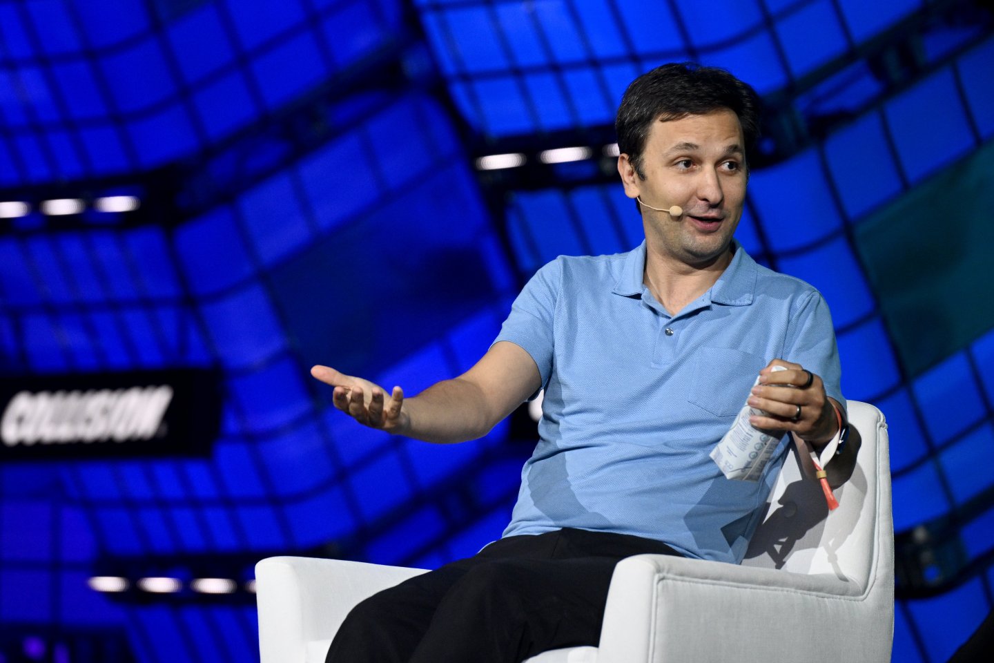 A seated man in a blue shirt gesticulating onstage